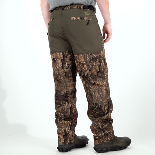 A person wearing MST Jean Cut Wader Pant, a camouflage trouser with adjustable waist and ankle adjustment. Features front slash pockets and zippered rear pocket.