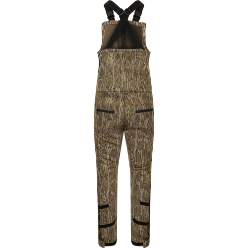 A brown overalls with black straps, featuring a four-way stretch material, gusseted crotch, and articulated knees for ease of movement. Includes Sherpa-lined slash handwarmer pockets, Magnattach™ left chest pocket, and zippered rear security pockets. MST Ultimate Wader Bib.
