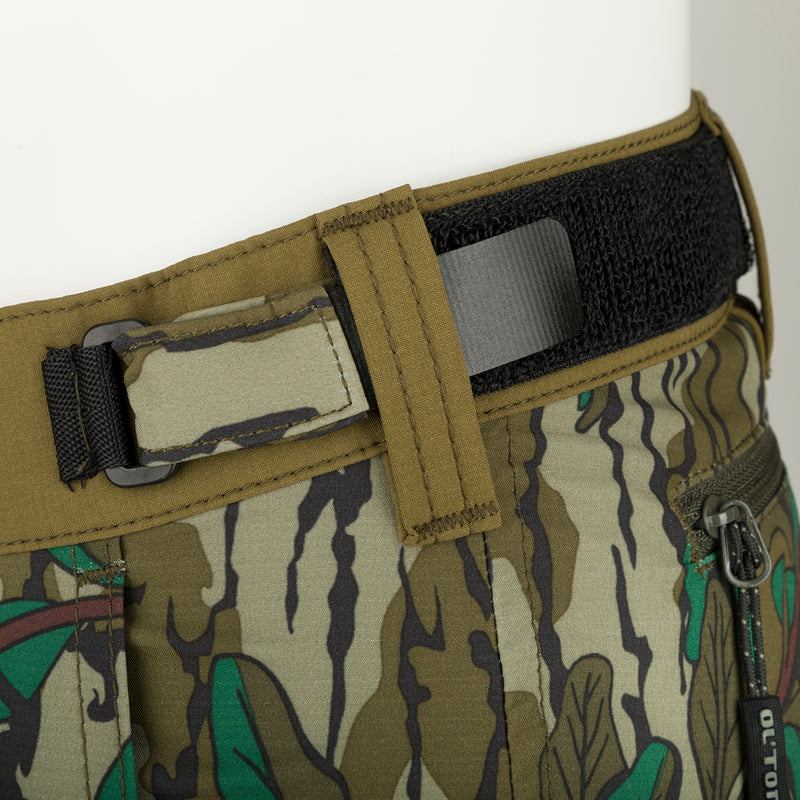 A close-up of the Youth Tech Stretch Turkey Pant, a lightweight and durable 4-way stretch pant designed for hunting. Features reinforced knees, ankles, and bottom, gusseted crotch for comfort, and adjustable waistband. Mesh and zippered pockets provide ventilation and storage.