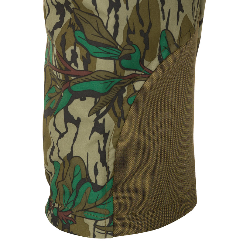 A close-up of the Youth Tech Stretch Turkey Pant, featuring a camouflage pattern on durable, moisture-wicking fabric. Designed for comfort and mobility with reinforced knees, ankles, and a gusseted crotch. Mesh and zippered pockets provide ventilation and storage. Perfect for hunting and outdoor activities.