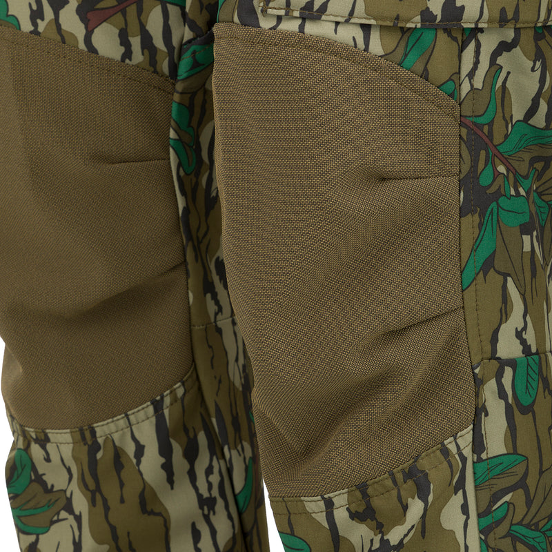 A close-up of the Women's Tech Stretch Turkey Pant, featuring a camouflage pattern. Designed for spring turkey hunting, these lightweight, moisture-wicking pants offer 4-way stretch and reinforced knees for durability. Stay comfortable and concealed in the woods with a relaxed fit and adjustable waistband. Mesh and zippered pockets provide ventilation and storage for hunting essentials.