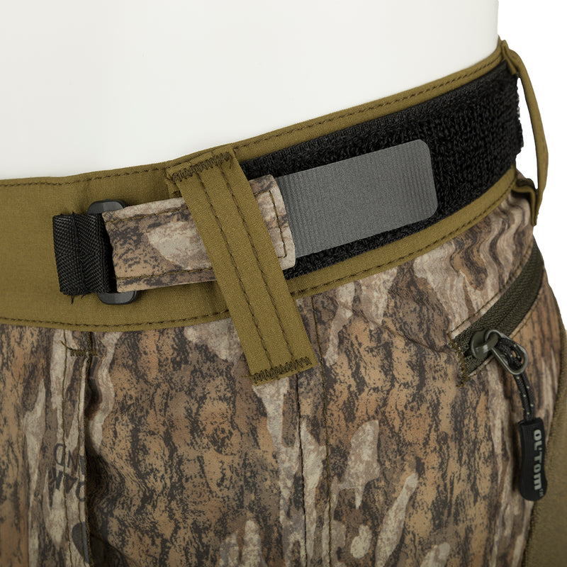 A close-up of the Men's Tech Stretch Turkey Hunting Pant, featuring a camouflage pattern, belt, and fabric strap. The pant is designed for spring turkey season, with reinforced knees, ankles, and bottom for durability. It has a relaxed fit, adjustable waistband, and multiple pockets for storage. Perfect for hunting and outdoor activities.