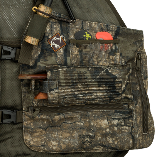 Time & Motion™ Gunslinger Turkey Vest: Close-up of bag and vest with logo, fabric, strap, and zipper. Perfect for organized hunting with 9 call pockets, detachable cords, and various compartments. Comfortable foam cushion, mesh back area, and adjustable straps. Lightweight at 3 lbs. 2 oz.